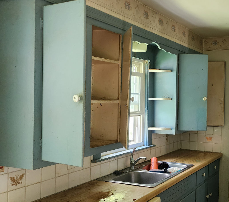 A kitchen before renovation with cupboard doors missing, a scuffed countertop and outdated paint colors